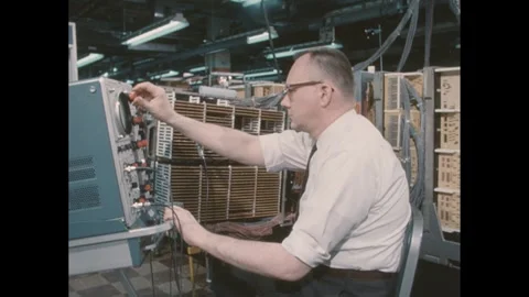 1960s: Man sits in room with computer servers in front of monitor with knobs and 스톡 동영상 276860721