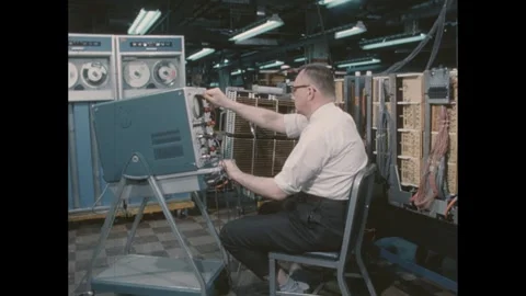 1960s: Man sits in room with computer servers in front of monitor with knobs and 動画素材 276860722