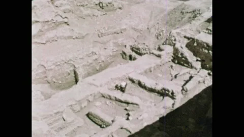1960s: Man stands looking at ancient ruins in city of Jericho. Sculpture of face Stock Footage 149640246