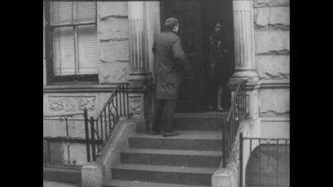 1960s: Man walks down a street. He walks up the steps and passes a woman coming Stock Footage 254264837