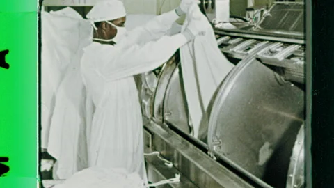 1960s: Masked worker puts laundry into industrial washing machine.  Man adds Stock Footage 155855000