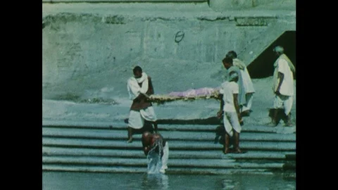 1960s: Men carry wrapped corpse down to river, dip corpse into river. Vidéo 126012126