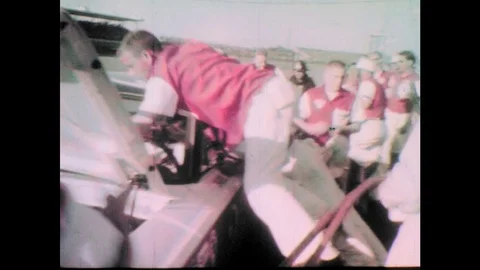 1960s: Men quickly work on race car on pit road.  Man adjusts tires.  Crew Stock Footage 77452204