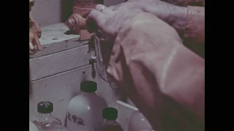 1960s: Men work in lab.  Men transfer water into containers and check gauges. Stock Footage 151606330