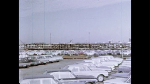 1960s: Pan across cars in parking lot. Men lift machinery in factory. Stock Footage 103558897