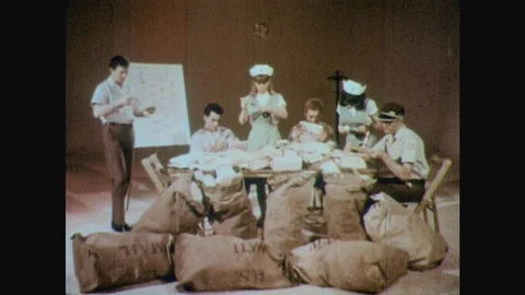 1960s: People sit at table surrounded by bags of mail.  Nurses feed men seated Stock Footage 123864168
