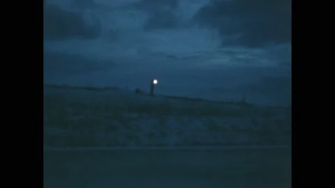 1960s: Person waves flashlight back and forth. Man sits at desk, reads from 스톡 동영상 217560051