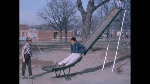 1960s: Playground, boy sits on slide, talks to friend, cracks knuckles, Stock Footage 238791339