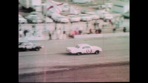 1960s: Race cars drive down pit road. Man waves down car. Driver motions for a Stock Footage