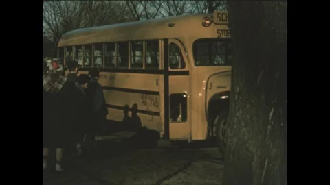 1960s: School bus pulls up to curb and kids board. Boy rakes leaves in yard. Stock Footage 243928395