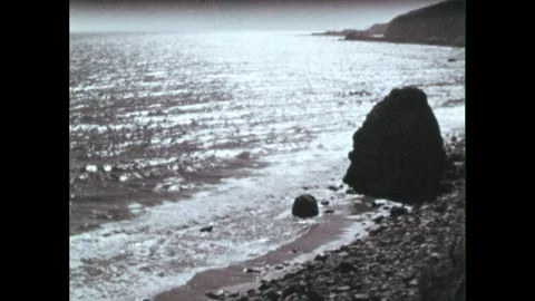 1960s: Seashells. Waves gently roll onto rocky shore. Clouds passing in sky. Stock Footage 259639500