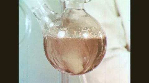 1960s: Solution bubbles in chemical apparatus. Man attaches glass tube. Hands Stock Footage