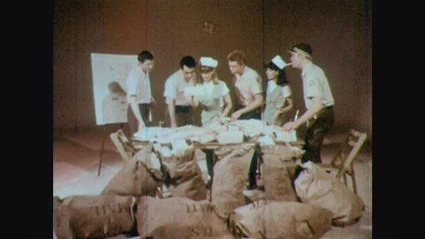 1960s: Table surrounded by bags of mail.  Young people grab and inspect Stock Footage 123864159