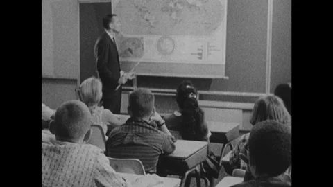 1960s: Teacher pulls down world map and uses pointer. Children listen and raise Stock Footage 102001552