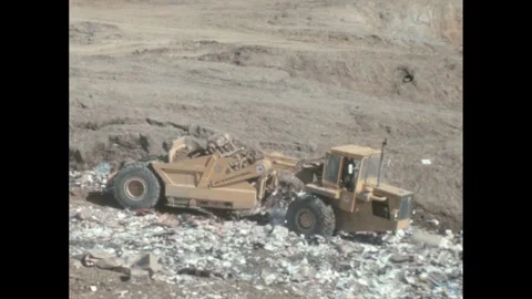 1960s: Truck pulling trailer, dumps dirt over garbage in landfill. Stock Footage 244535727