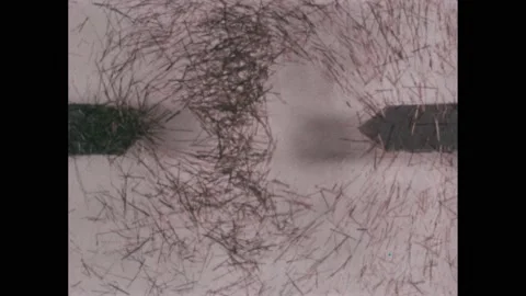 1960s: Two charged rods under glass repel hairs in lines of force. Text Stock Footage 221103411