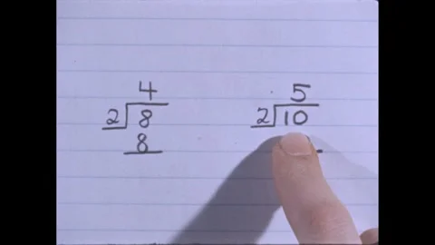 1960s: Two division problems on the paper, finger pointing to each of them. Stock Footage 273114033