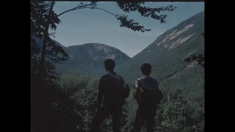 1960s: Two men hiking in forest stop to look at view then keep hiking. Stock Footage 277613393