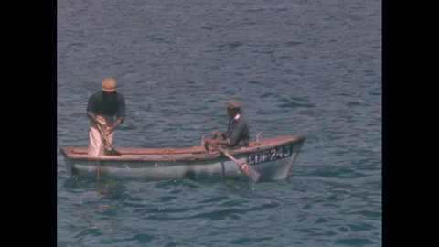 1960s: Two men in a small boat, one man pulls up a fishing net. Stock Footage 277655348