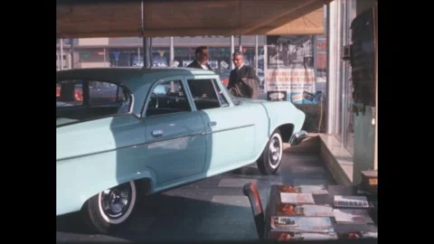 1960s: Two men talk while looking at car in showroom. Stock Footage 273066384