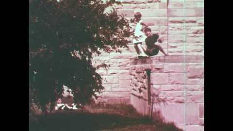 1960s: UNITED STATES: boy jumps from wall. Girl jumps. Man walks across Stock Footage