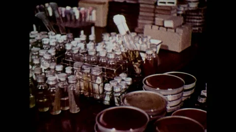 1960s: Vials, test tubes and petri dishes on counter. Two scientists at work. Stock Footage 127731968