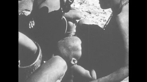 1960s: Woman breastfeeds baby while others eat from bowl. Man cuts legs off dead Stock Footage