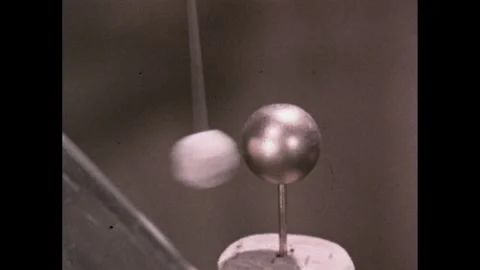 1960s: Wool ball on string moves between glass tube and Leyden jar. Man sits at Video stock 280054644