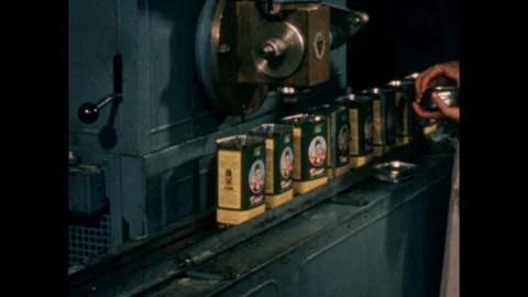 1960s: Worker adding cans to the filling machine, lids placed on top. Stock Footage 258142524