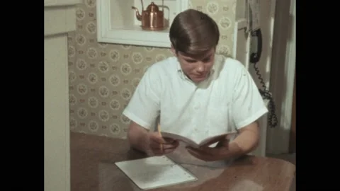 1960s: Young man sits at table, reads pamphlet, makes notes. Person holds up 库存影片 194489413