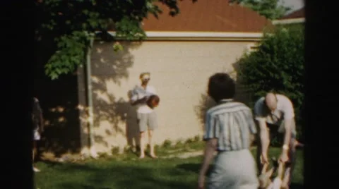 1962: man picks child up by wrists and ankles, then swings him around as people Stock Footage