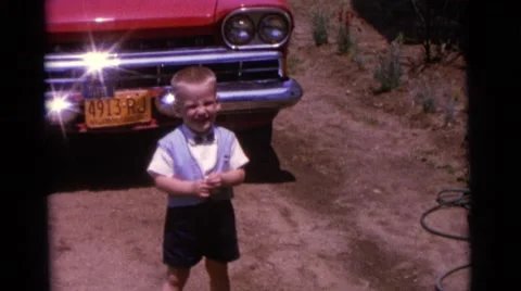 1963: Two Children Laughing While Playing in a Field Near a Red Wagon CAMDEN Vídeos de archivo 67824487