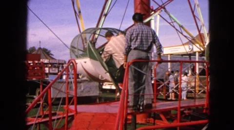 1963: young men enter rock-o-plane ride at amusement park and attendant locks Stock Footage
