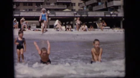 1964: children play in a body of water on a sunny day with lots of people Stock Footage