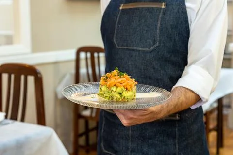A waiter holding a plate with a salmon tartare with avocado and mango on it xkwx tartare, avocado, mango, fancy, appetizer, food, delicious, gourmet, tasty, waiter, meal, fresh, plate, snack, dish, hands, background, cuisine, eat, cream, restaurant, closeup, baked, healthy, lunch, dinner, nutrition, elegant, homemade, decoration, slice, sauce, fruits