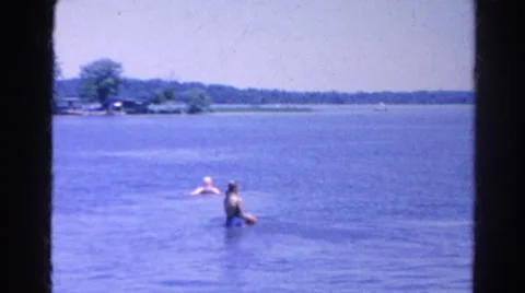 1966: father and mother and two female children throwing red ball in lake Stock Footage