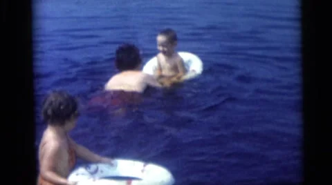 1967: children taken in inner tubes at the lake to practice swimming with mother Stock Footage