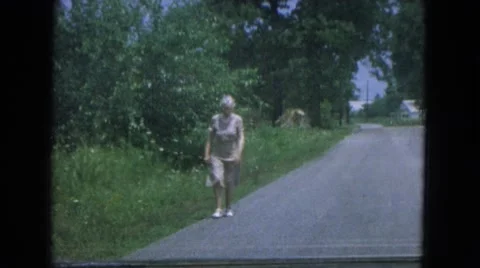 1967: an older woman wearing a light brown dress walking down the road. NEVADA Stock Footage
