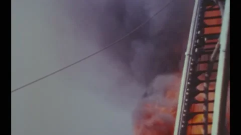 1968 - Firemen on tall engine ladders use hoses to fight a raging fire on a Stock Footage 246306009