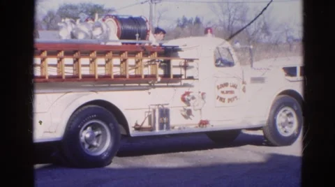 1968: an old fire engine parked by the roadside with a fireman standing Stock Footage