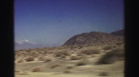 1969: Driving Through a Dry Desert with Patches of Grass and a Small Mountain Video stock 67732616