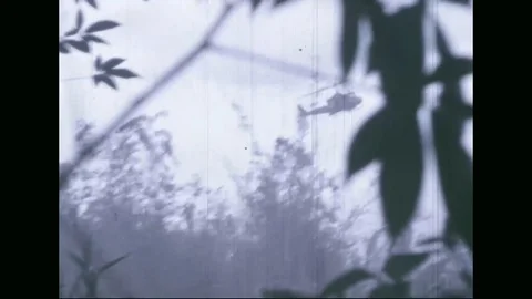 1969 - US Army helicopters attack enemy positions in Vietnam while soldiers make Stock Footage 115802846