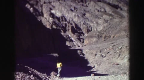 1969: woman in yellow shirt and blue jeans sits on rock near mountain path Stock Footage