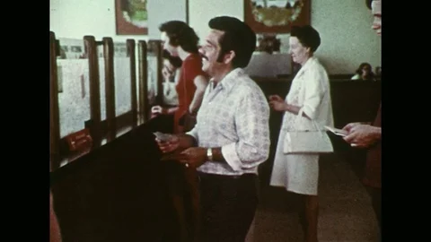1970s :  At the bank, a young man stares as an older man cashes his check. Stock Footage