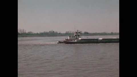 1970s: Barge moves bins of coal up river. Man operates controls and sails barge Stock Footage 232327853