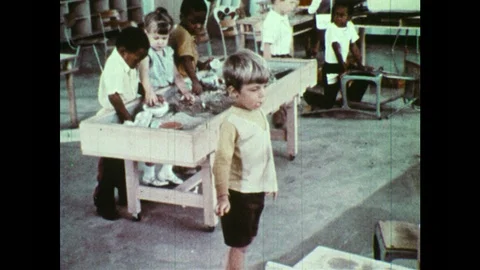 1970s: Boy opens cabinets and knocks over paper cups. Boy tries to knock ball Vídeo Stock 93327178