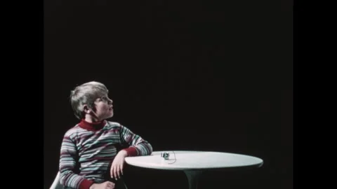 1970s: Boy sits at table with timer on it and talks to someone off-camera. Boy Stock Footage 248620437