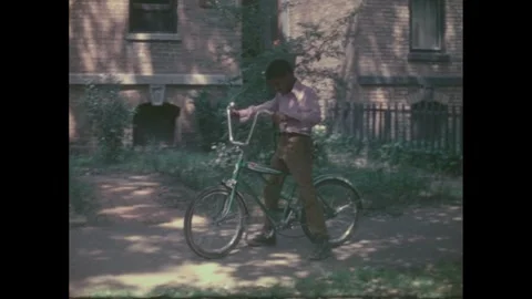 1970s: Boy walks a bicycle down a sidewalk. He lays the bicycle down. The chain Video stock 276198674