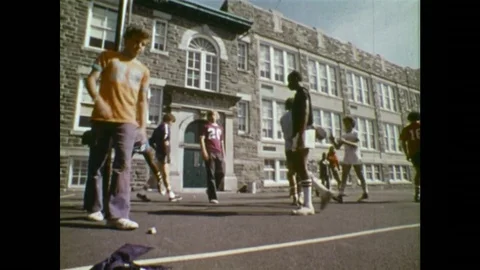 1970s: Boys walk. Boy picks up jacket from ground. Boy gives jacket to other Stock Footage