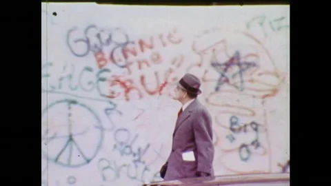 1970s: Businessman walks in front of graffitied wall. Young man spray paints Stock Footage